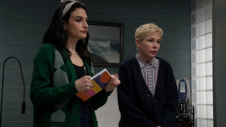 Nikki holding a book and wearing a green cardigan standing next to Molly who is in a dark Blue Cardigan. 