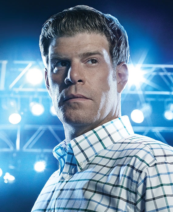 Stephen Rannazzisi headshot in white checkered button down, standing to the side with bright stadium lights in background