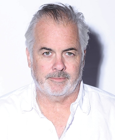 Peter OFallon headshot in plain white button down with bright light casting shadow on plain white background