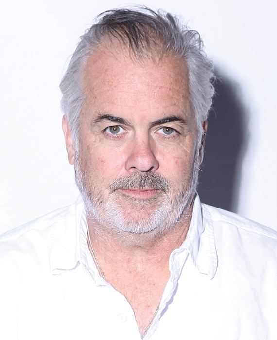 Peter OFallon headshot in plain white button down with bright light casting shadow on plain white background