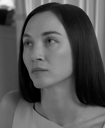 Black and white headshot of Sydney Lemmon as Lauren Bessette in FX's Love Story wearing a square cut blouse.