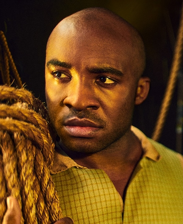 Austin Smith headshot in yellow checkered shirt, holding bundle of rope on right shoulder and looking over to the side 