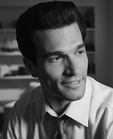 Headshot of Paul Anthony as John F. Kennedy Jr. in FX's Love Story in a suit with his hair slicked back.